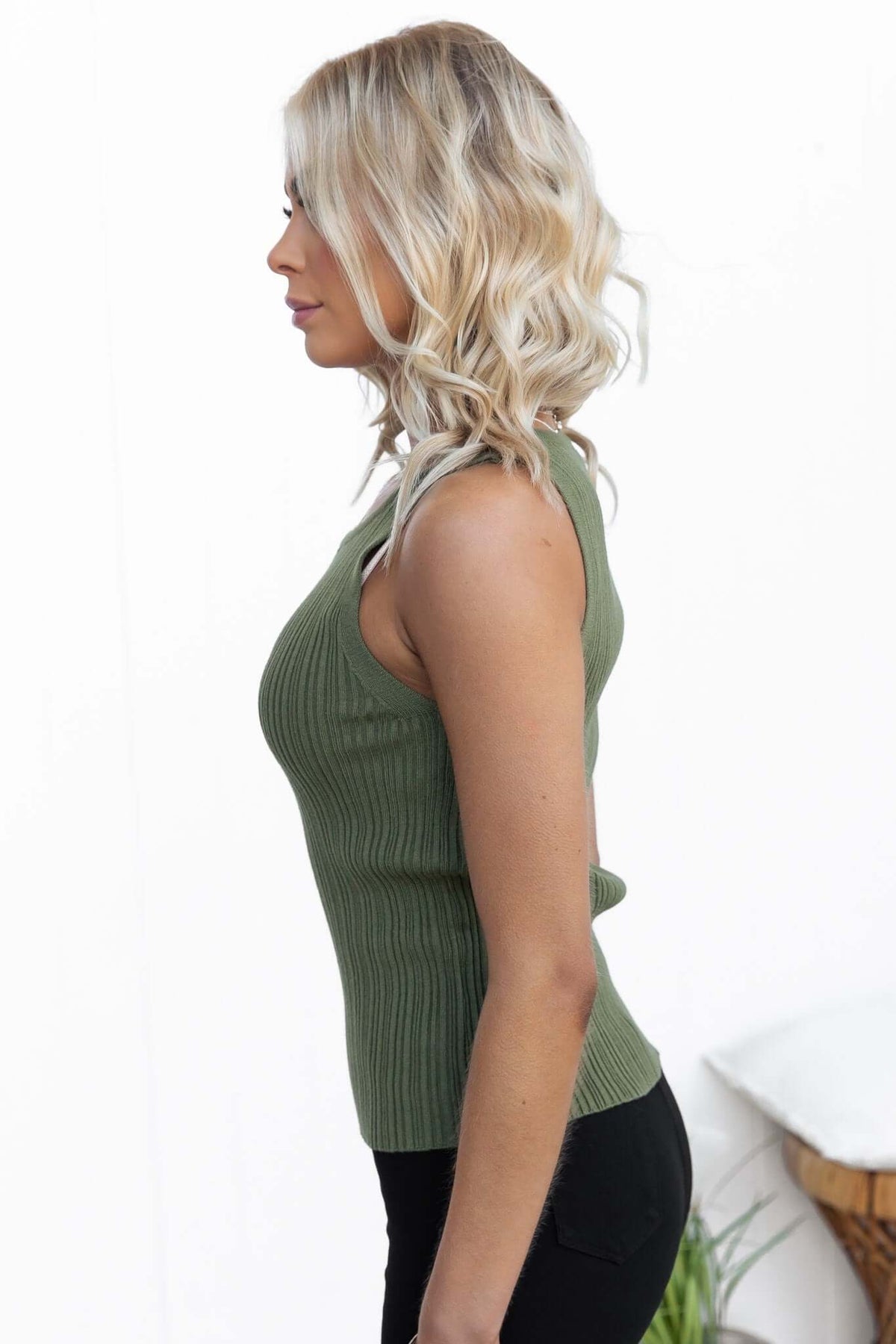 Side view of a woman wearing a green ribbed knit tank top, showcasing a round neckline and slim fit.