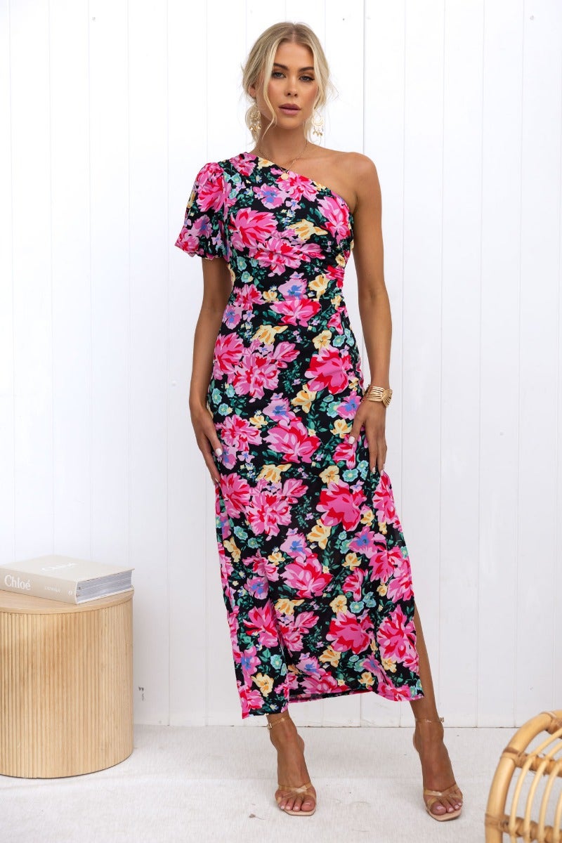 Karana Maxi Dress with black floral print, one-shoulder neckline, side split and ruching detail, styled on a model.