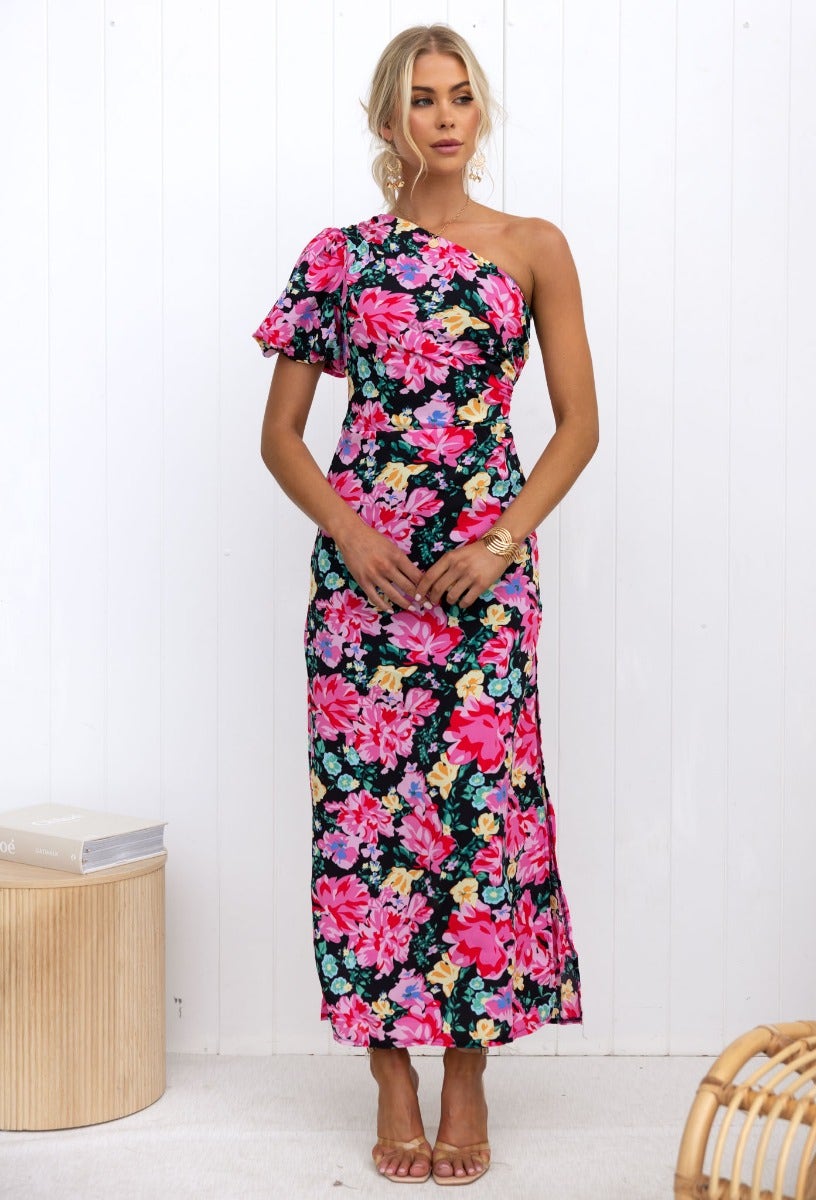 Model wearing Karana Maxi Dress, a floral black and pink one-shoulder maxi dress with ruching and a side split.