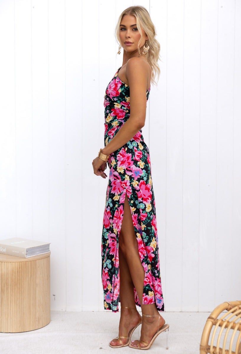 Model wearing a black floral print Karana Maxi Dress with one-shoulder neckline and side split.