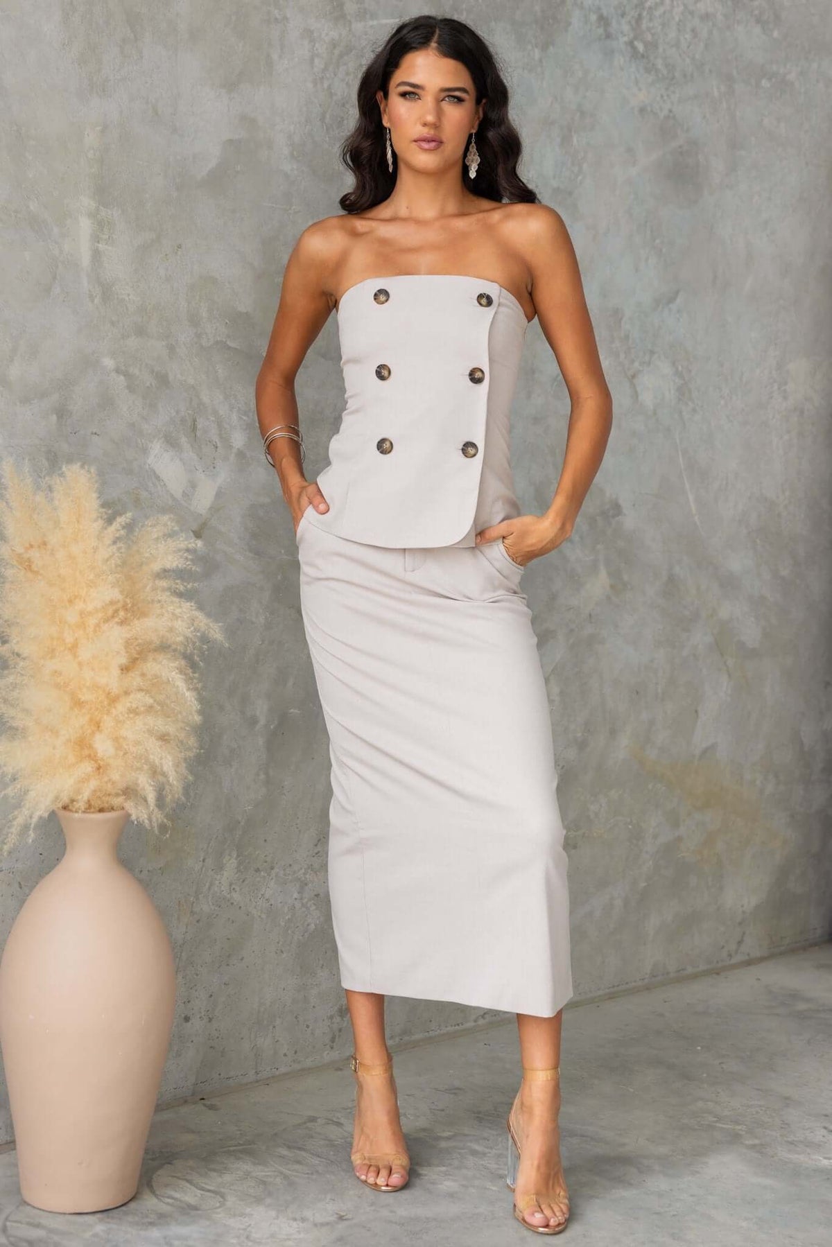 Model wearing a strapless Lanetta Top with decorative buttons, paired with a sleek skirt on a textured background.