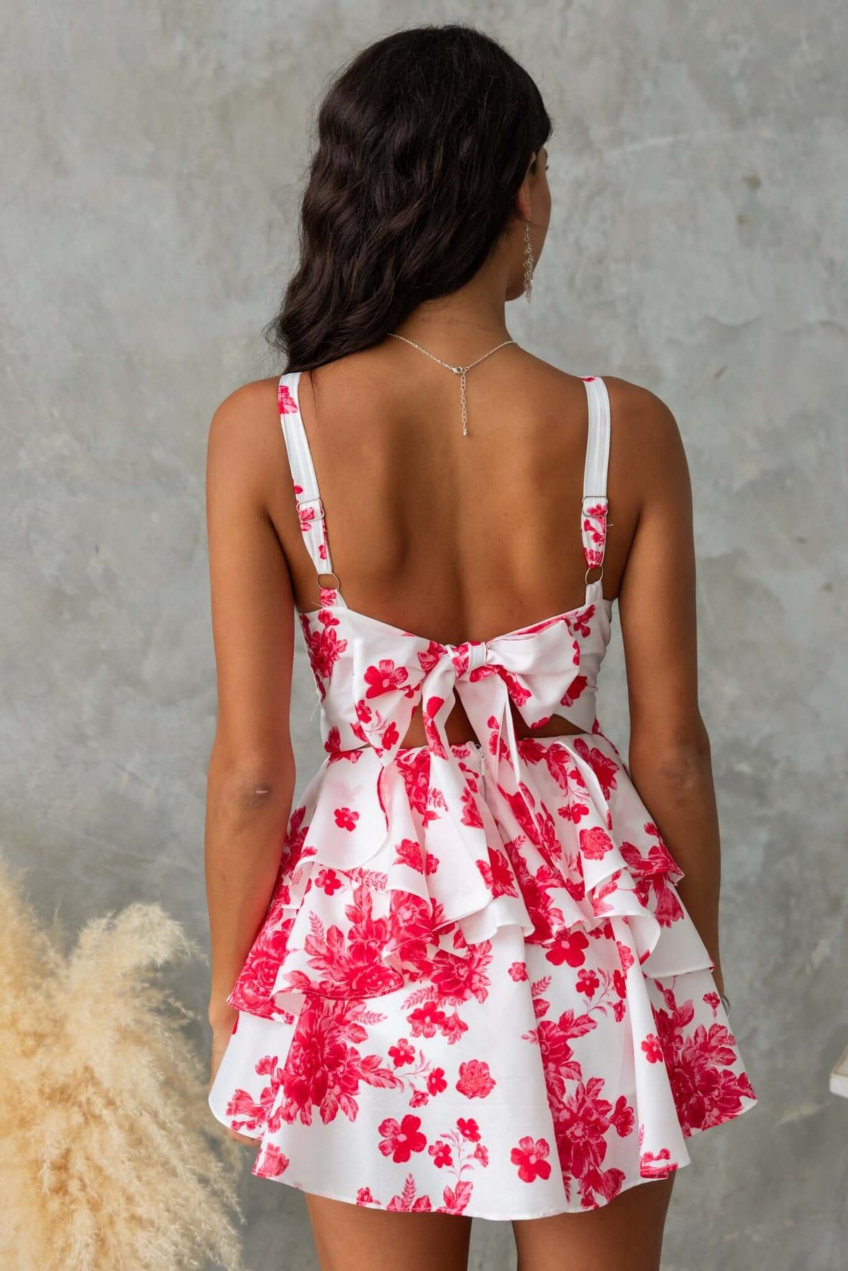 Back view of a floral playsuit with adjustable straps and a tie at the back, featuring a layered ruffle design.