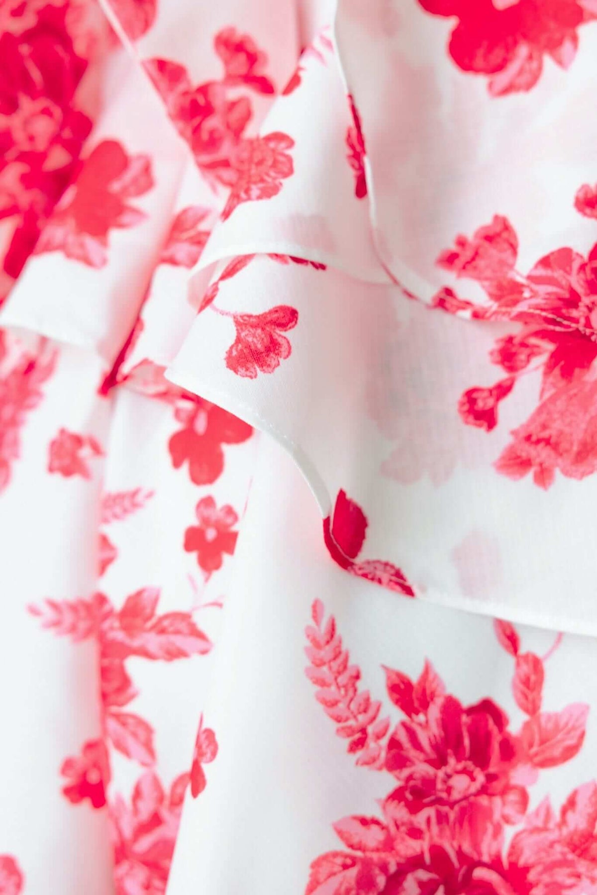 Close-up of floral ruffle detail on By Your Side Playsuit, showcasing vibrant red flowers on a light background.