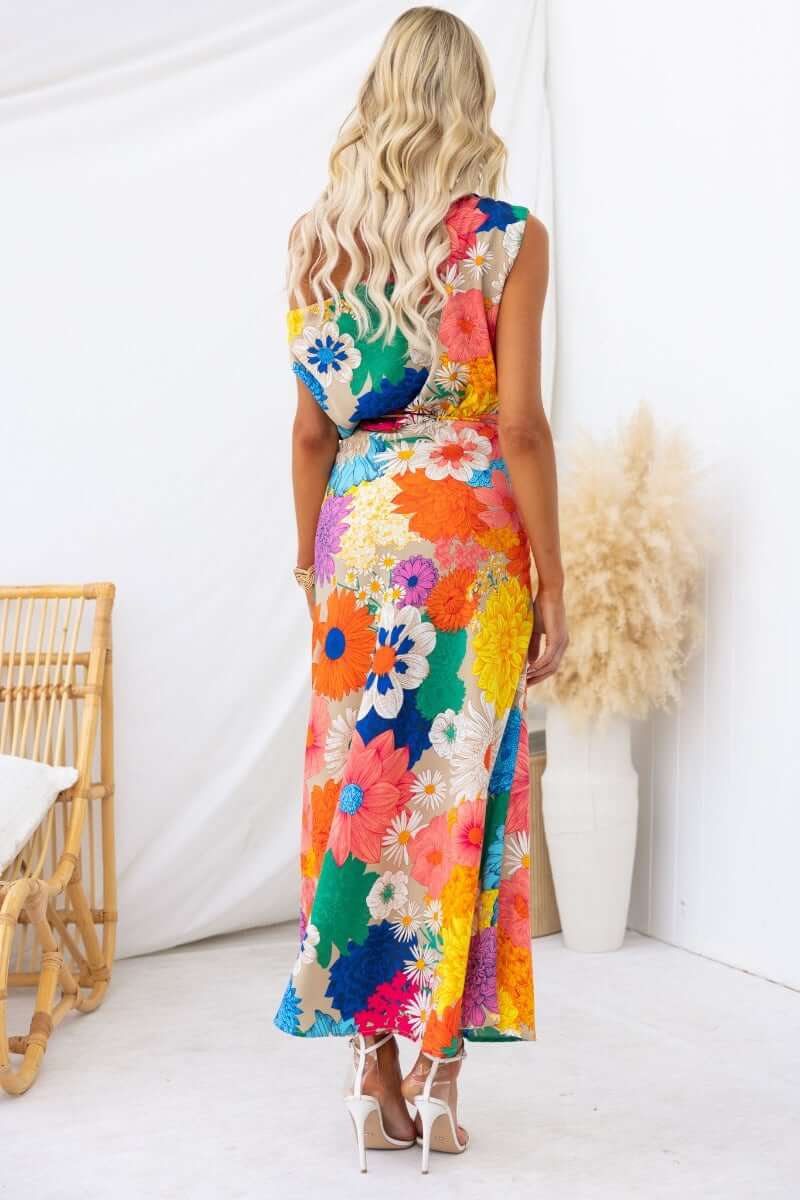 Woman wearing a colorful floral print maxi dress, showing the back design with a split at the front.