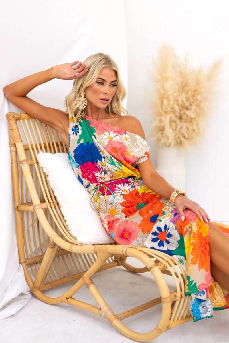 Model showcasing the Sicilian Sun Maxi Dress with vibrant floral print, seated elegantly in a rattan chair.