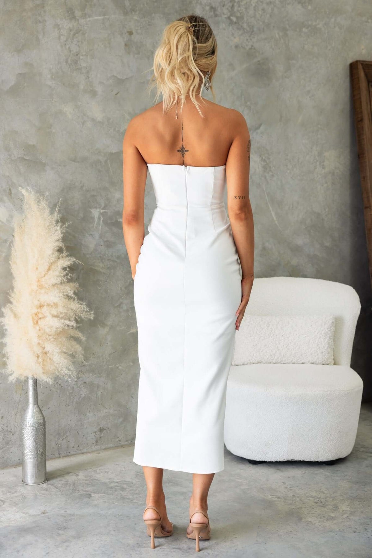 Back view of a model wearing a glossy strapless midi dress with an invisible zip and boning, showcasing a sleek design.