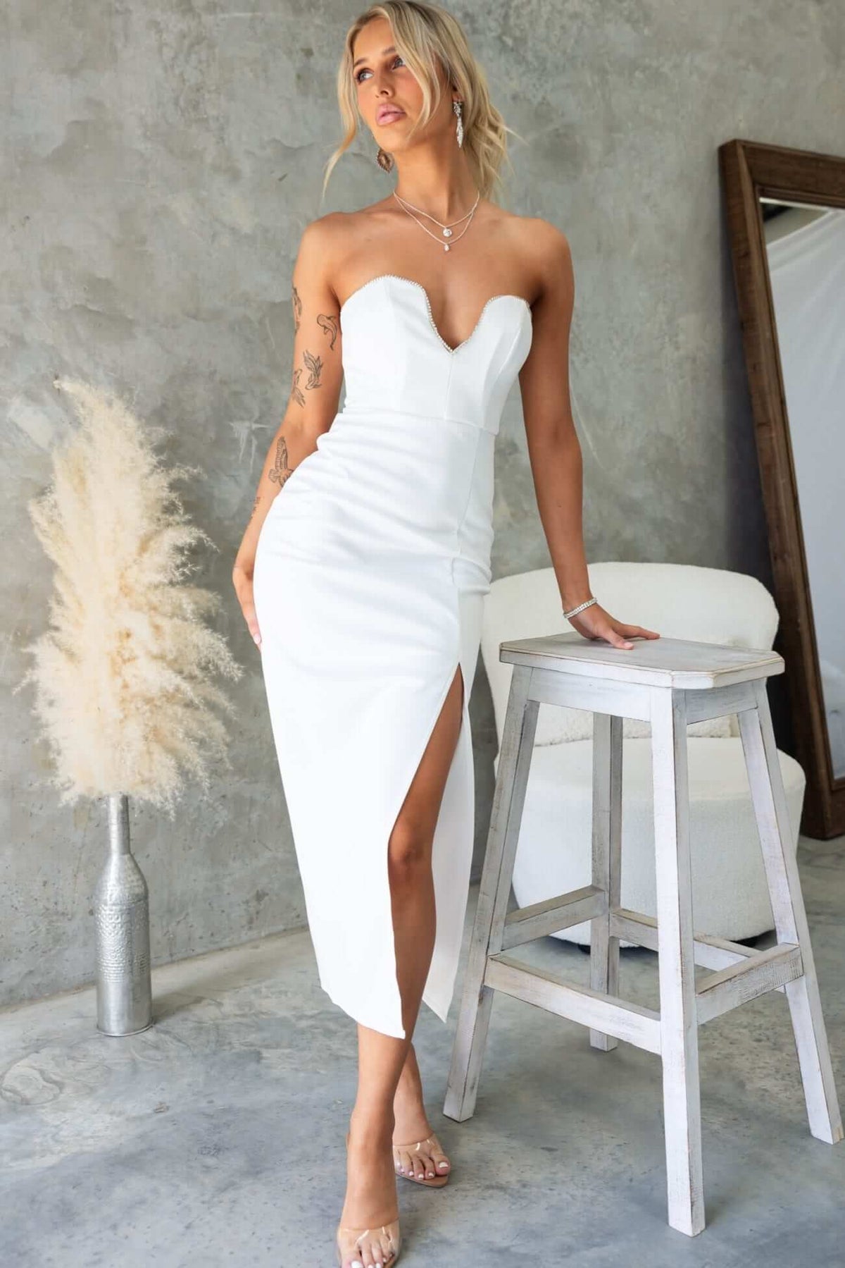Model wearing a strapless glossy white midi dress with a front split and diamante detail.