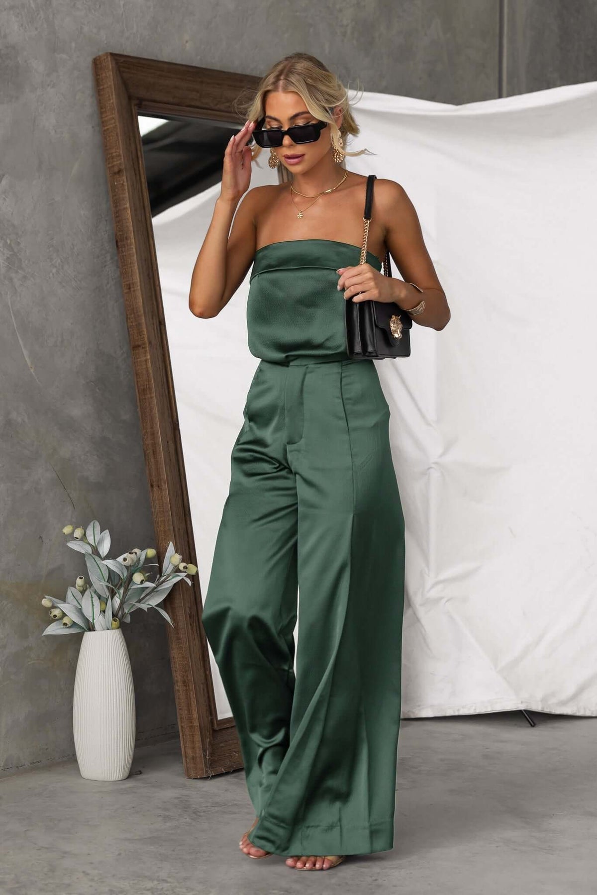 Woman wearing green Hampton style pants with a fitted top, accessorized with sunglasses and a bag, posed elegantly.