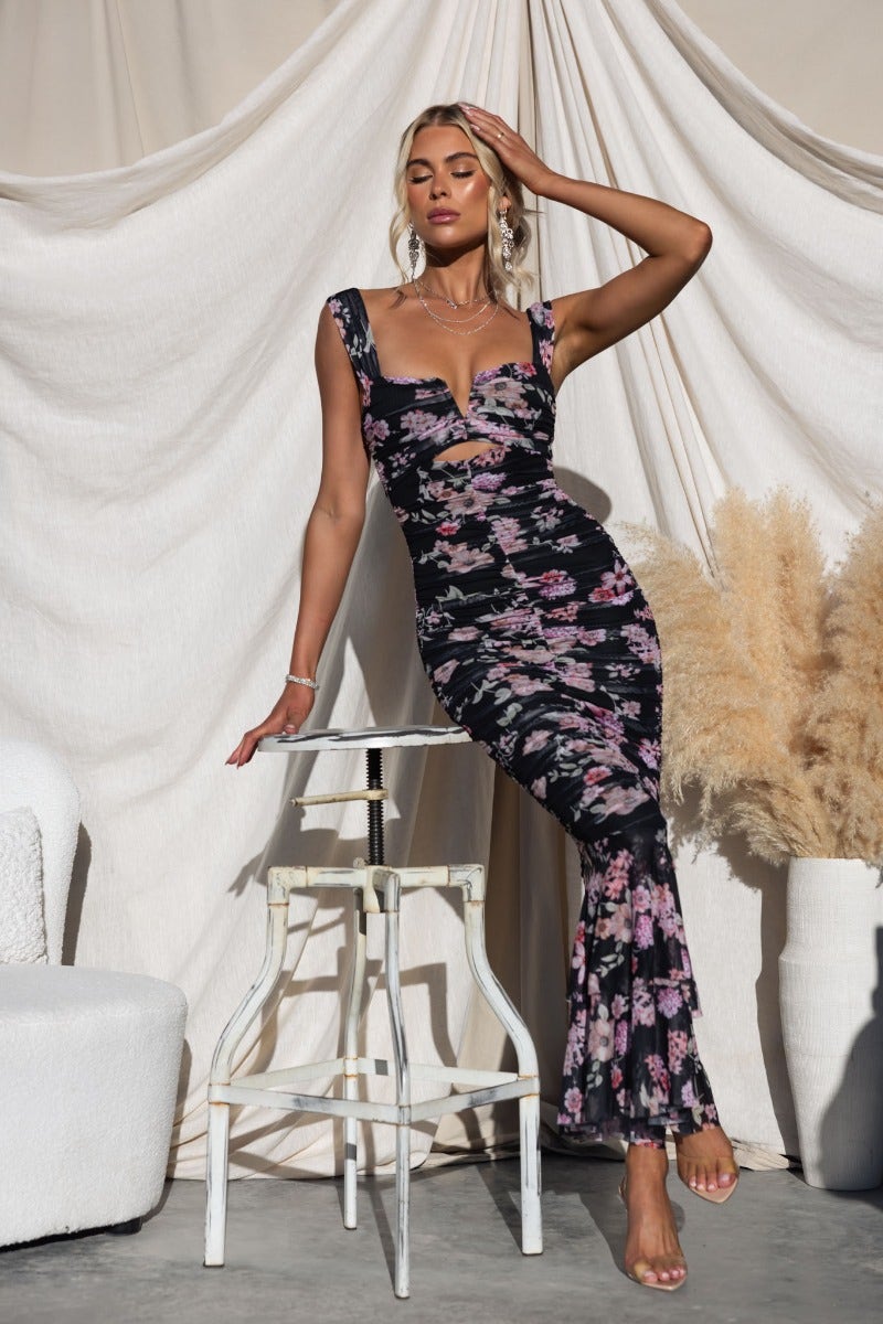 Zachia Maxi Dress in black mesh with floral design, featuring V-wire bust and ruched details, styled with a chic pose.
