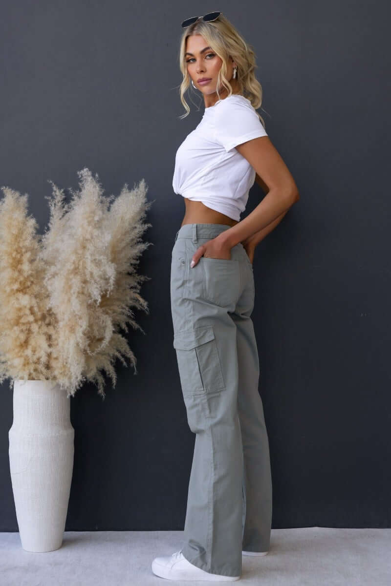 Model wearing Bowie cargo pants with a white crop top, styled against a dark background with decorative plants.