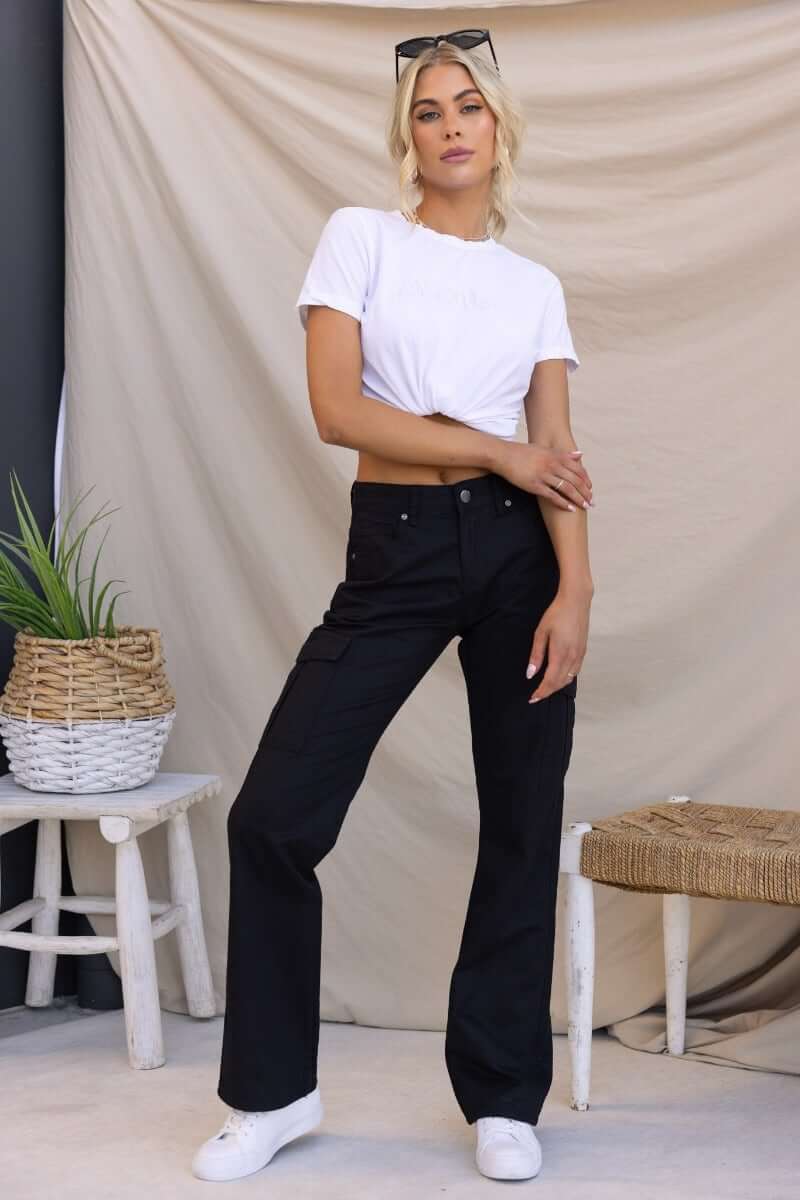 Model wearing Bowie Cargo Pants with a white crop top, showcasing black cargo pants with pockets and a relaxed fit.