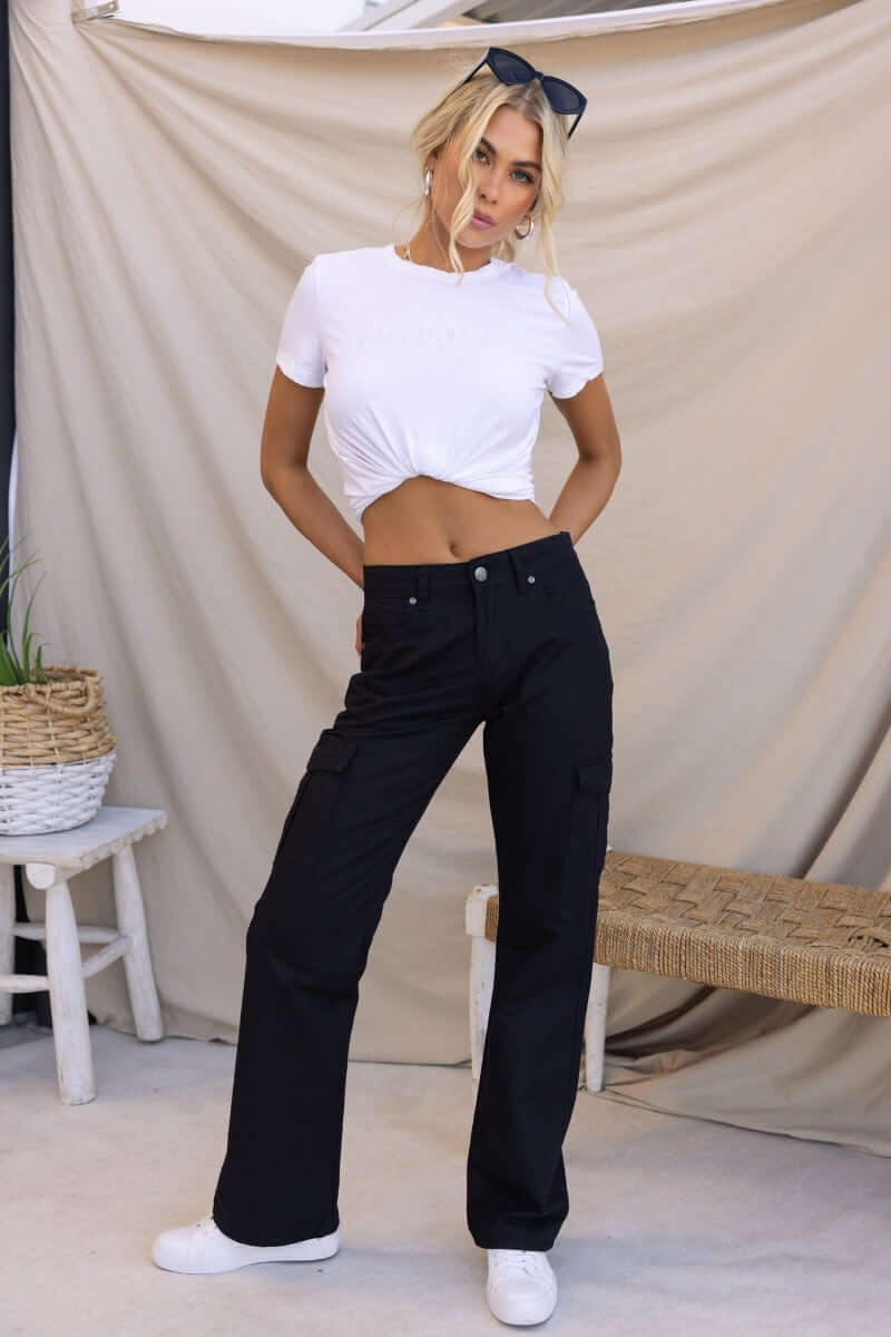 Model in black Bowie cargo pants paired with a white cropped t-shirt, showcasing fashionable relaxed fit and stylish pockets.