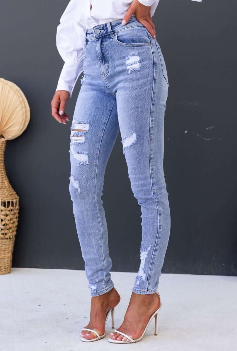 Model showcasing Mecka Jeans in distressed light blue denim with mid-high waist and front/back pockets.