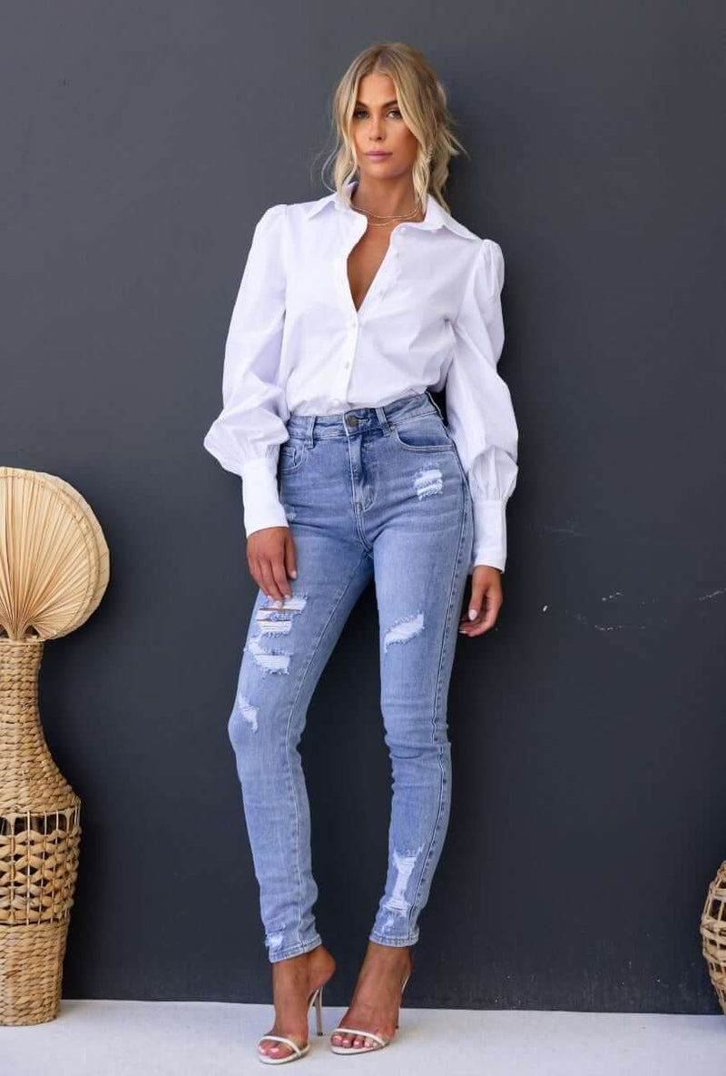 Model wearing Mecka Jeans featuring mid-high waist, distressed rips, and front/back pockets in light blue denim.