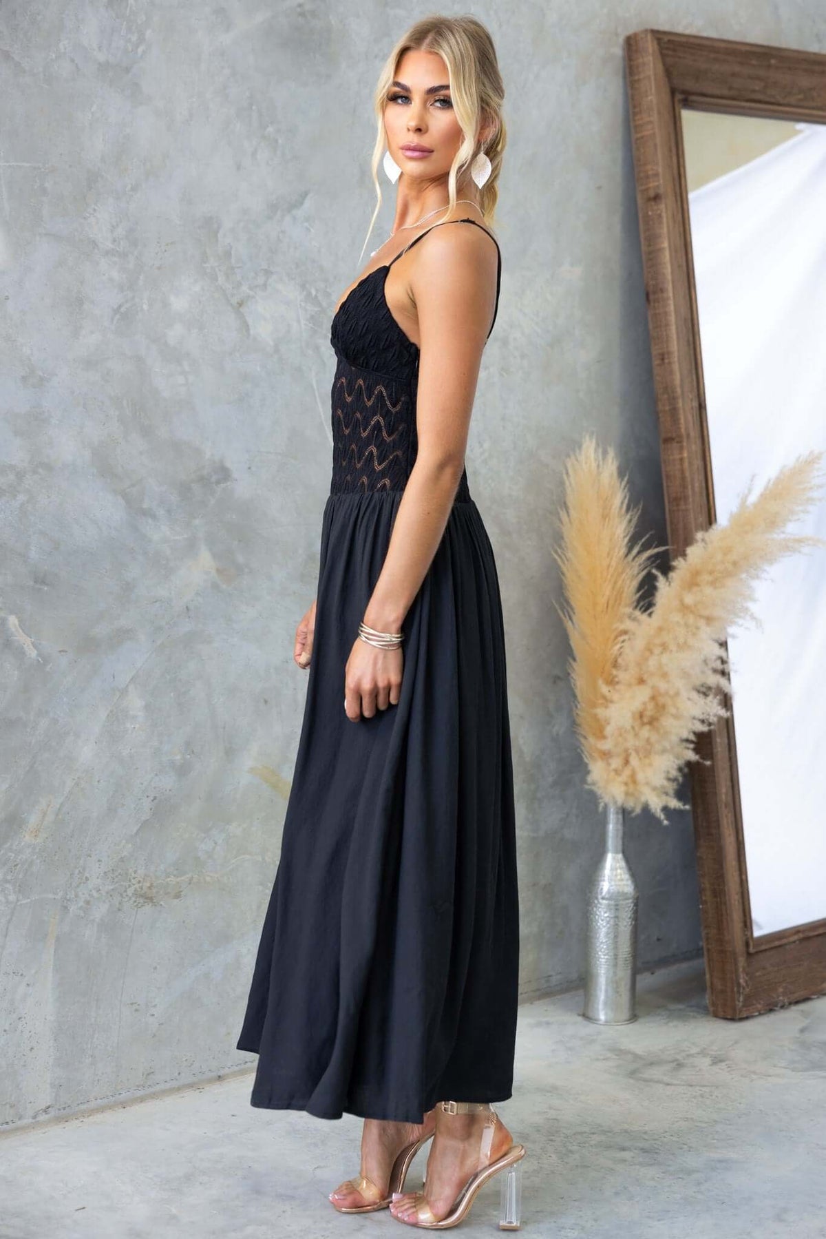 Elegant black Thaisa maxi dress with lace bodice and adjustable straps, styled with a mirror and decorative plants.