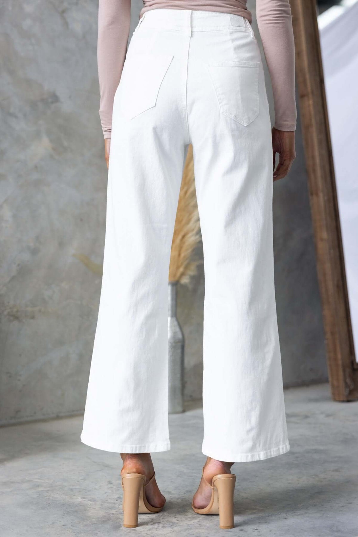 Back view of Blanca Jeans featuring a mid-high waist, wide legs, and pockets, styled with a fitted top and heels.