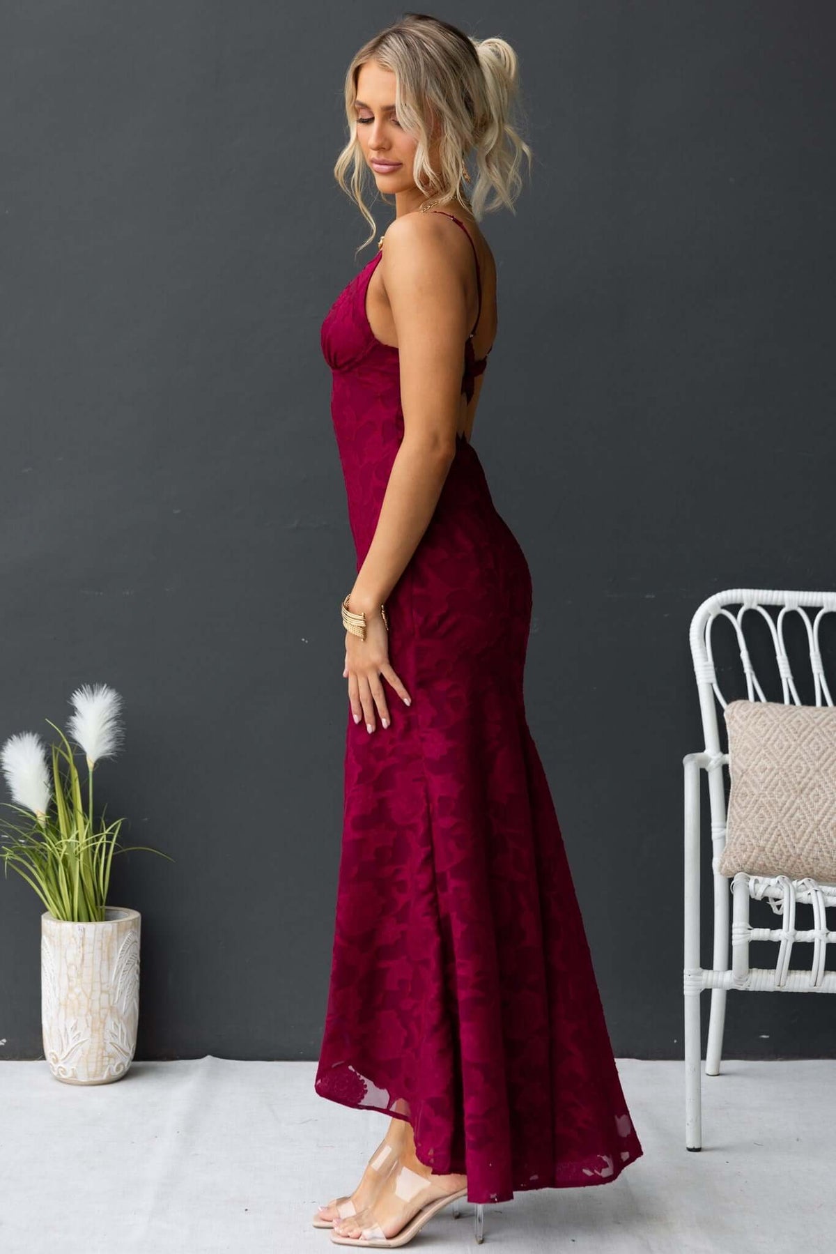 Side view of a woman in a burgundy Fontana Maxi Dress with adjustable straps and high-low hem.