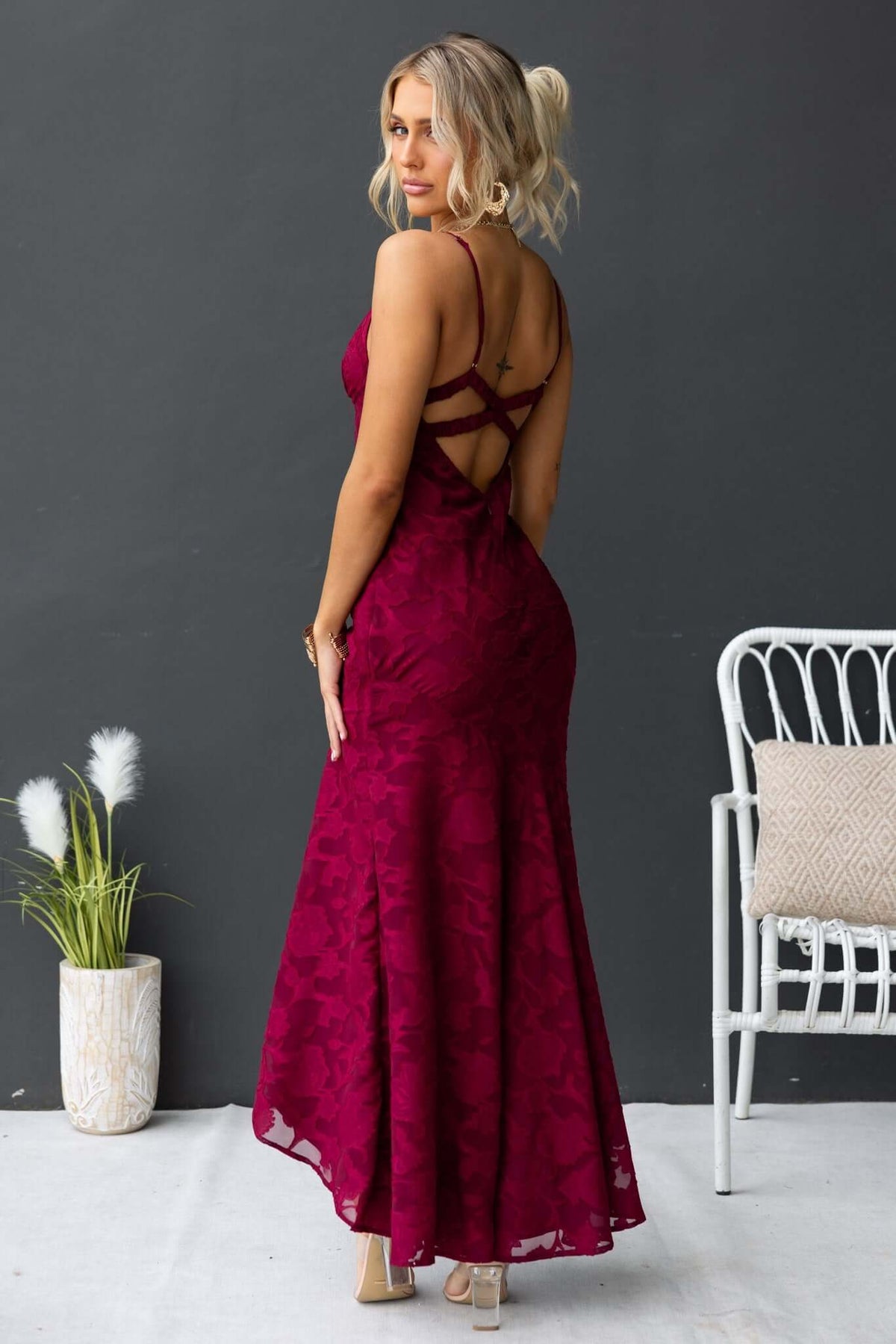 Back view of a woman wearing a burgundy Fontana maxi dress with adjustable straps and a high-low hem.