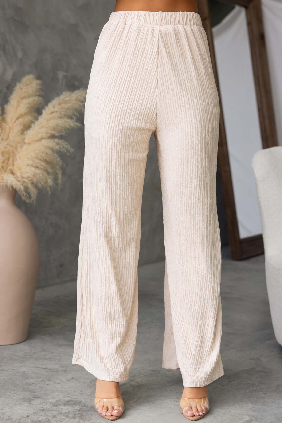 Lisa Pants in beige with a mid-high waist and elastic waistband, styled in a modern interior setting.