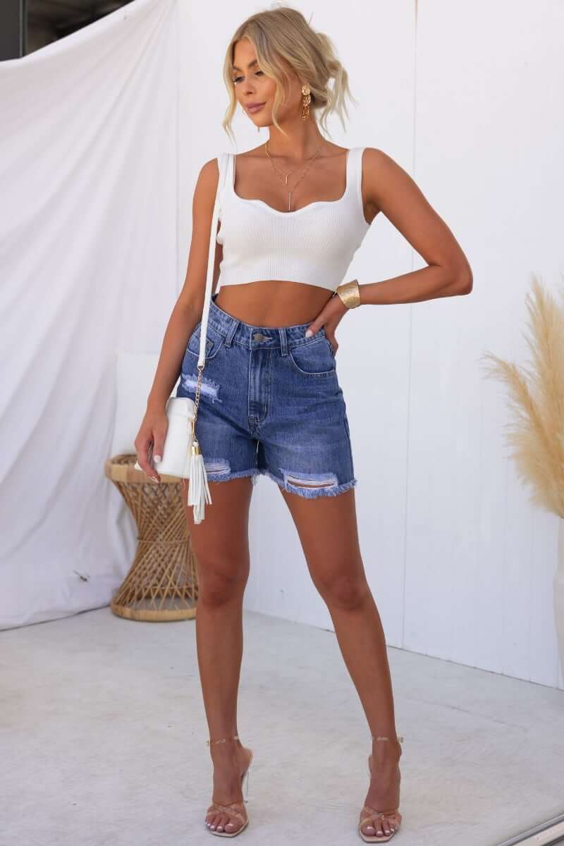 Model wearing Kobe Denim Shorts with distressed details and frayed hemline, styled with a white crop top and sandals.