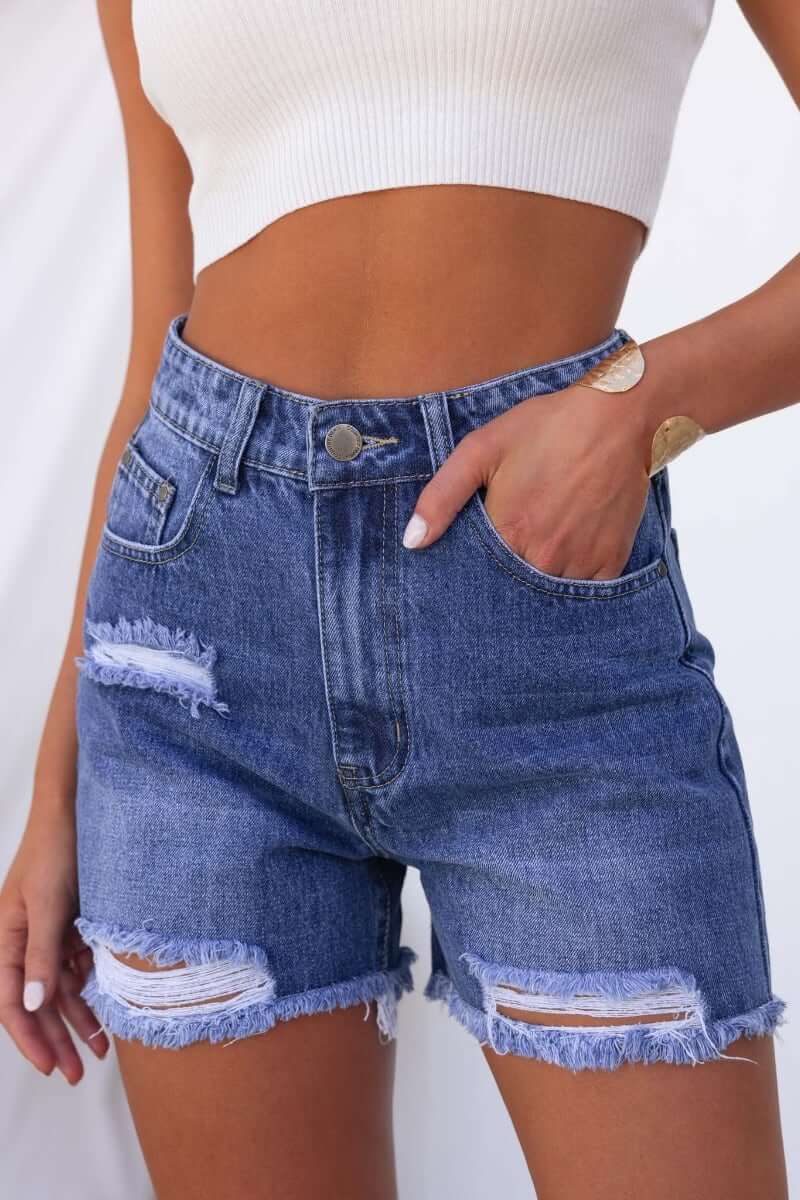Kobe Denim Shorts featuring distressed rips, frayed hemline, and pockets, styled with a fitted crop top.