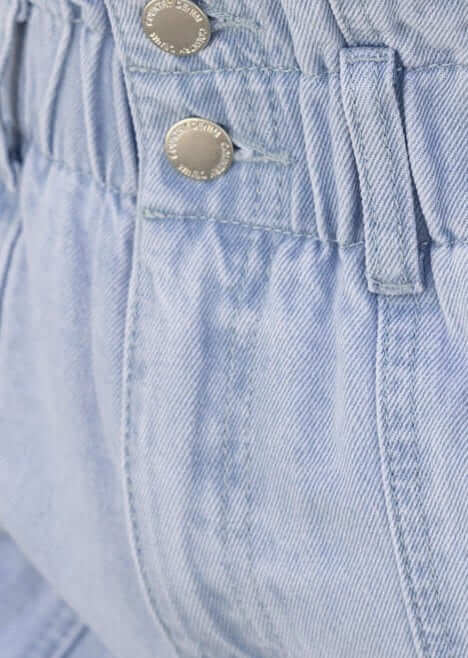 Close-up of Hattie Paper Bag Shorts showing the denim fabric, elastic waistband, and button closure.