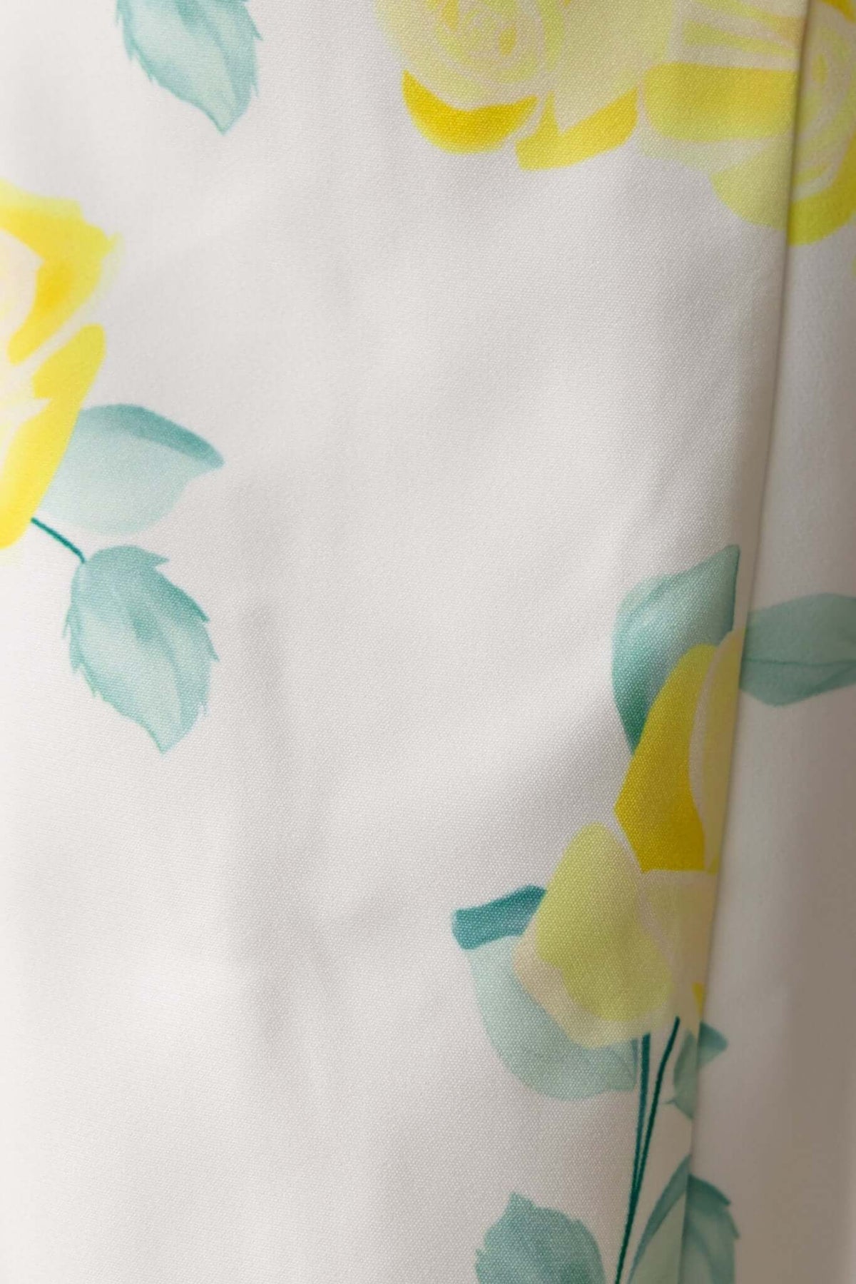 Close-up of yellow and teal floral pattern on a white background, showcasing the textile design of a demure dress.