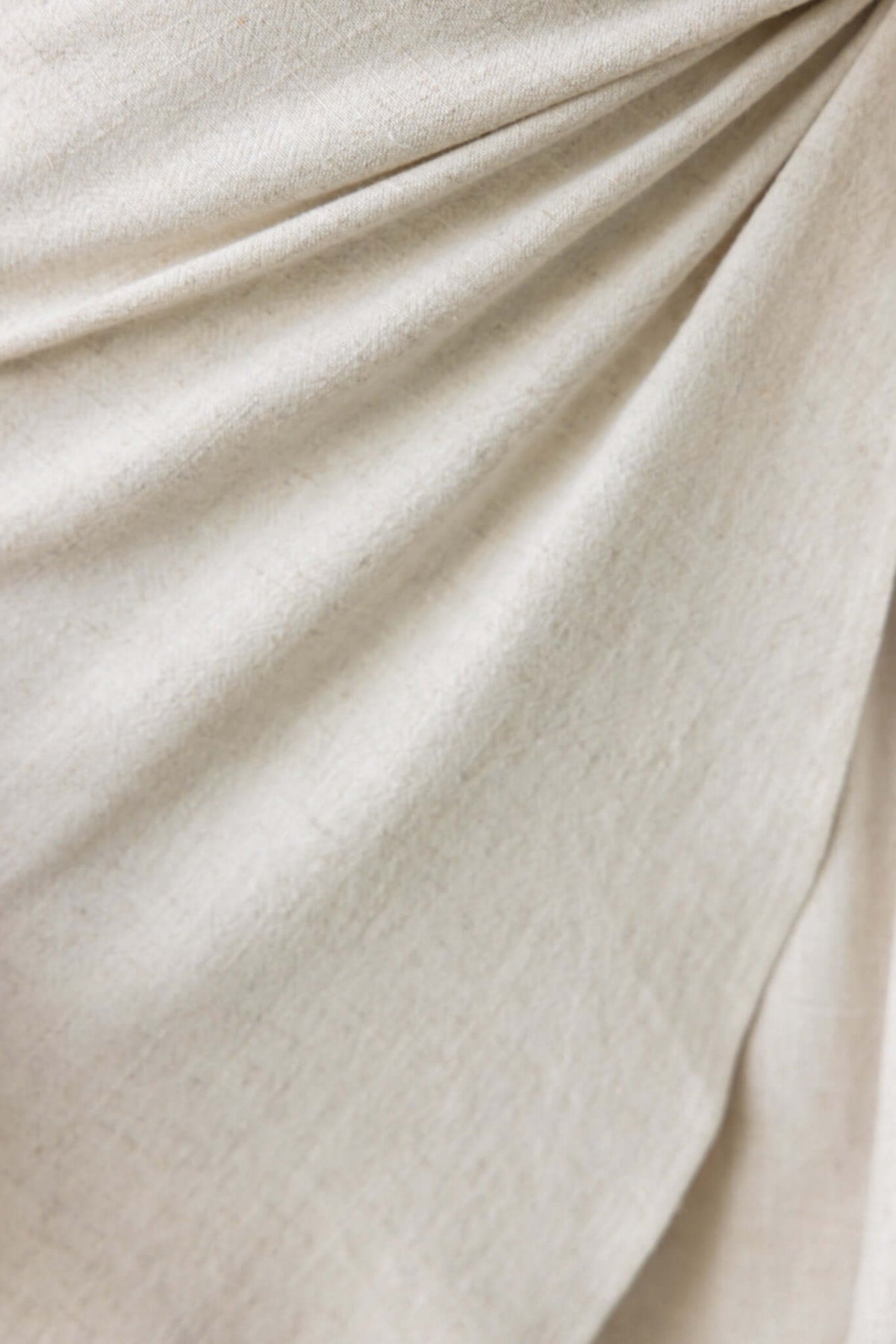 Close-up of soft beige linen fabric showcasing draped texture and detail, perfect for elegant dress designs.