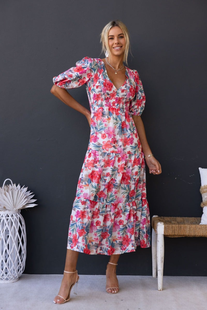 Woman in floral print Ave Maxi Dress with V-neckline and puff sleeves, styled in a modern setting.