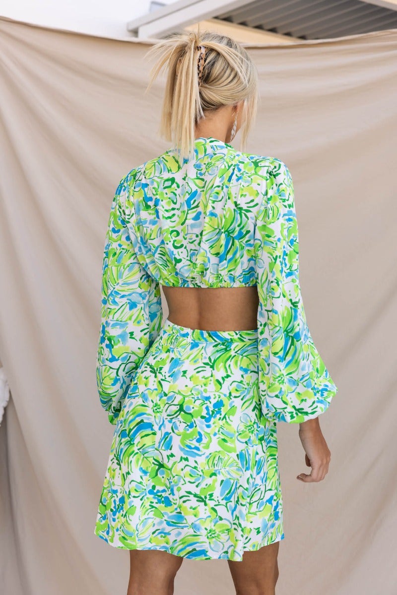 Model wearing a floral print Warm Embrace Dress with a deep plunge neckline and cut-out waist, featuring vibrant green and blue colors.