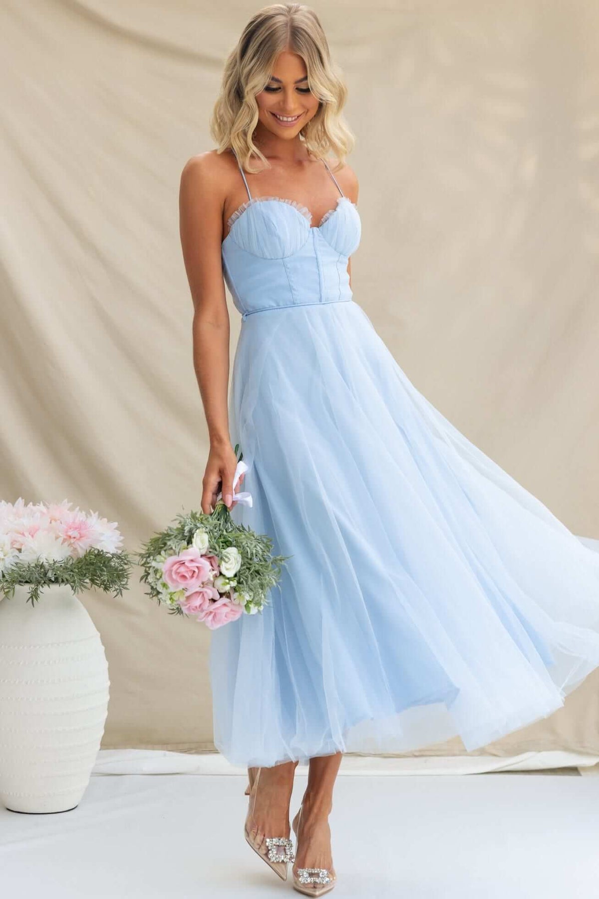Model wearing a light blue Florence Midi Dress with adjustable straps and a flowing tulle skirt, holding a floral bouquet.