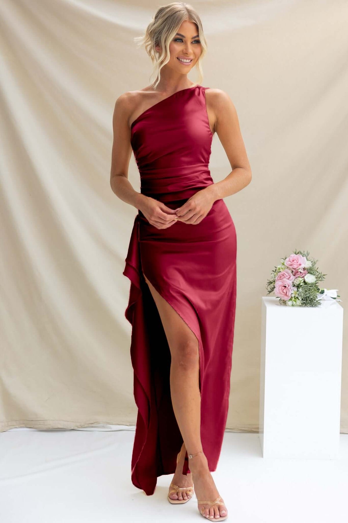 Model wearing Amaroso Bridal Dimmi Maxi Dress, a one-shoulder satin gown with ruffle trim and a thigh-high slit.