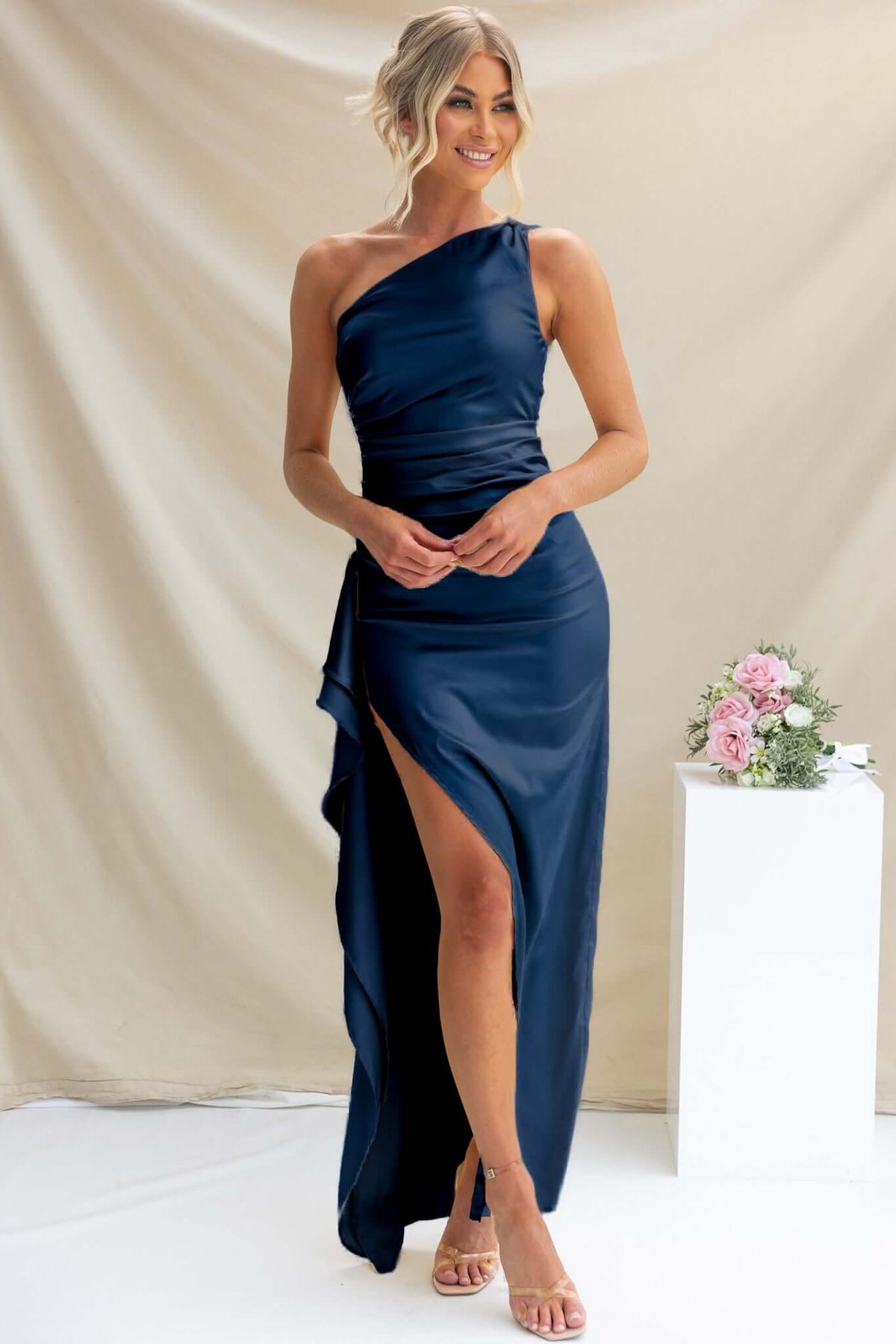 Navy satin Dimmi maxi dress with one-shoulder neckline and asymmetrical hemline, model posing elegantly.