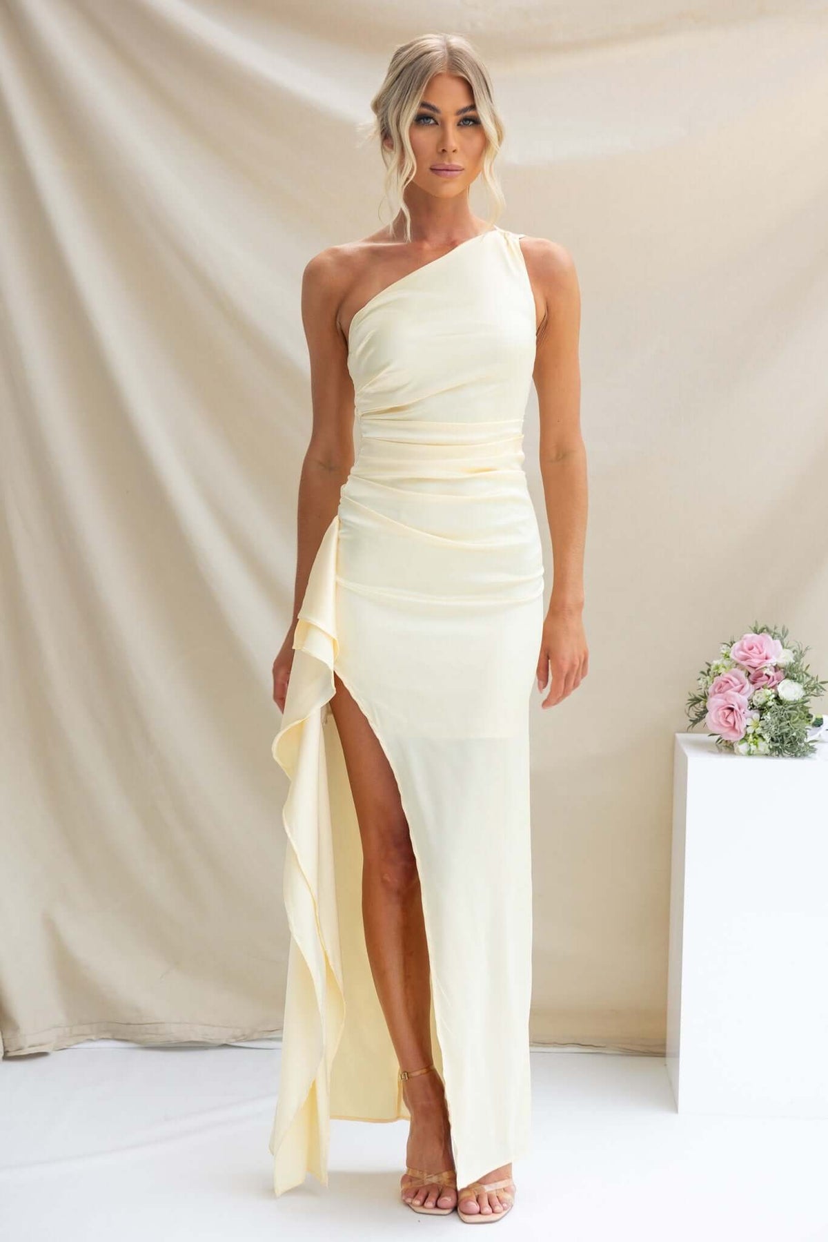 Dimmi Maxi Dress in soft yellow featuring a one-shoulder neckline, asymmetrical hemline, and ruffle trim.
