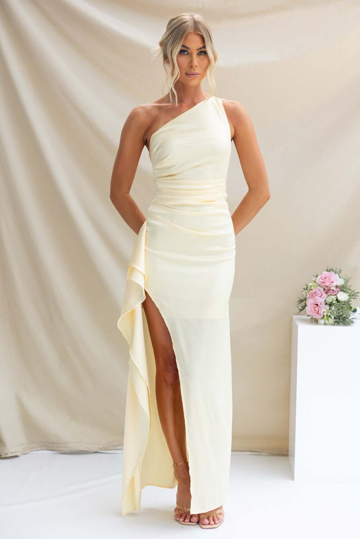 Model wearing a Dimmi Maxi Dress, a satin one-shoulder gown with a thigh-high split and ruffle trim.