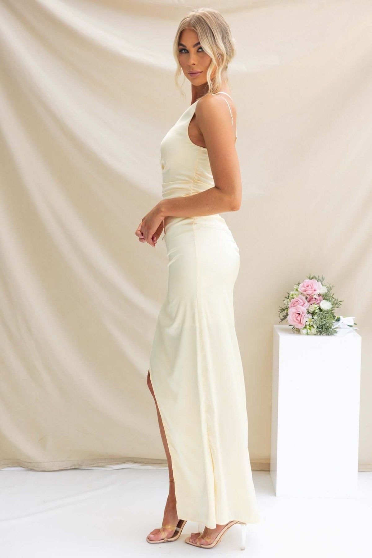 Model wearing Dimmi Maxi Dress in soft yellow, showcasing one-shoulder design and asymmetrical hemline.