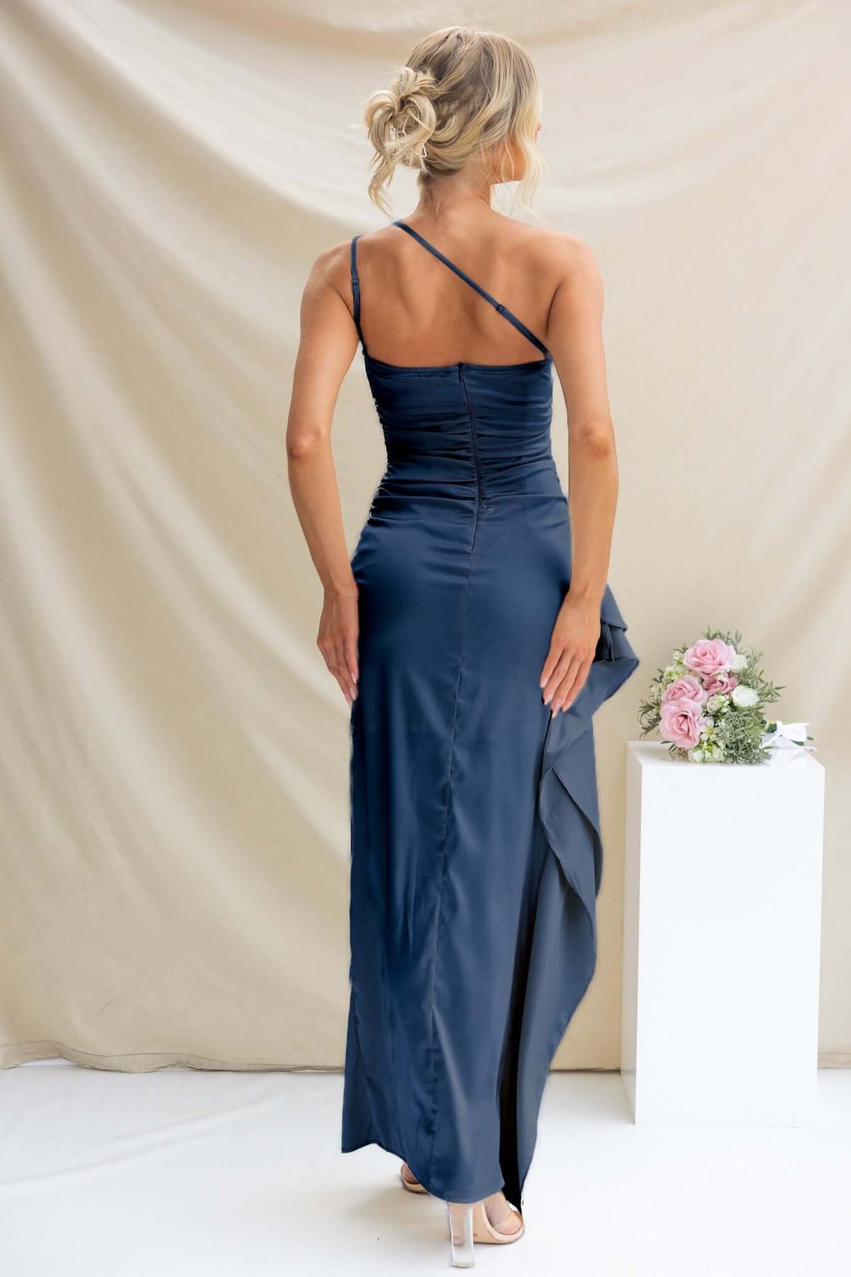 Back view of Dimmi Maxi Dress in navy satin showing adjustable straps and asymmetrical hemline with ruffle trim.