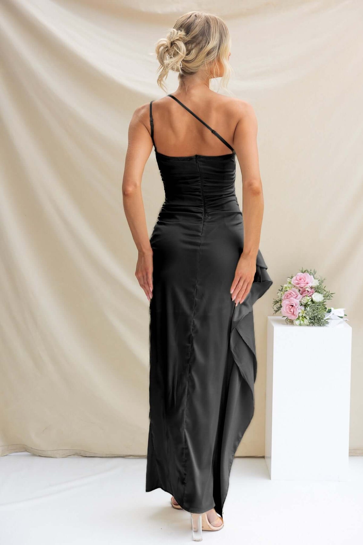Back view of the Dimmi Maxi Dress in black satin with one-shoulder neckline and ruffle trim.