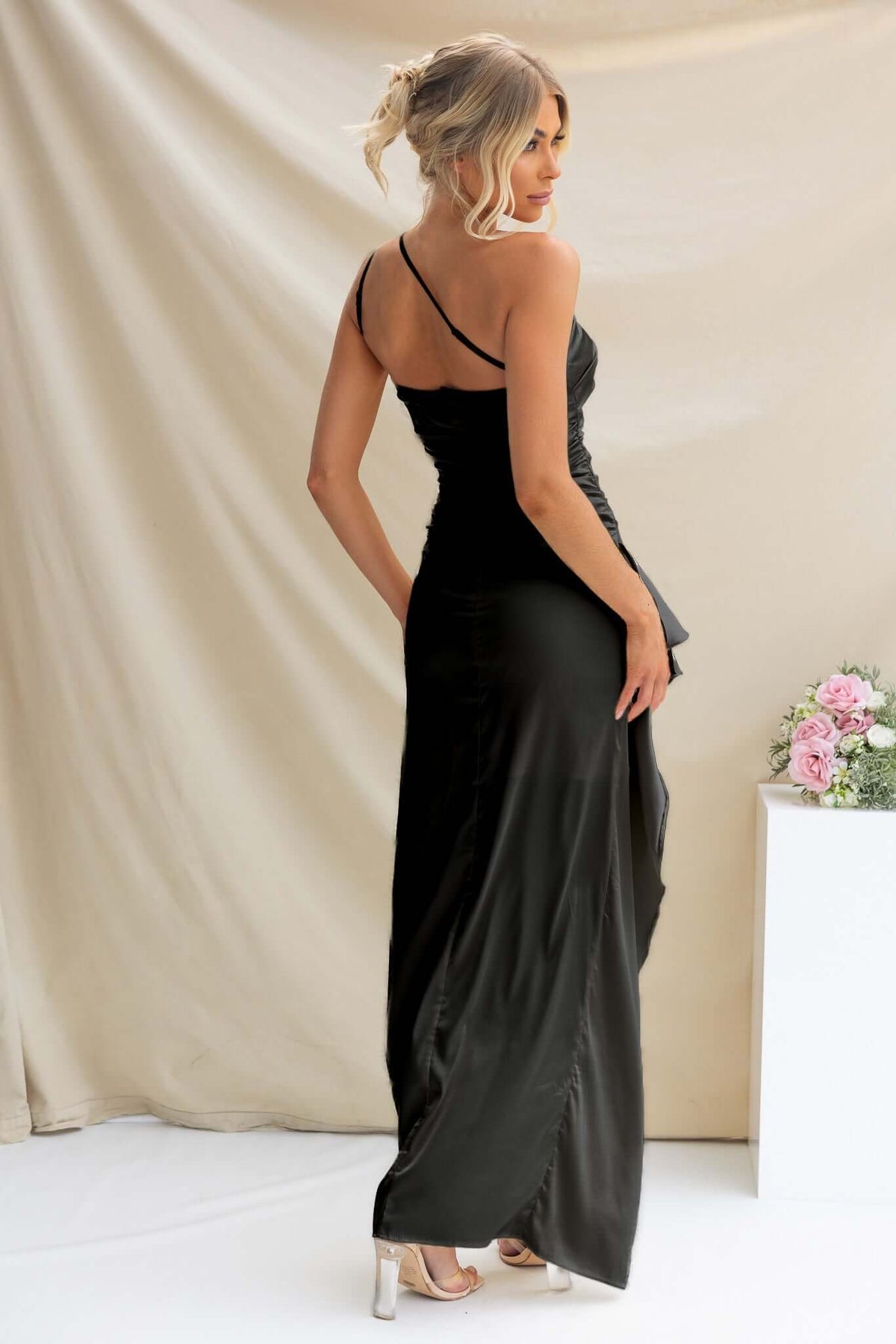 Back view of Dimmi Maxi Dress, a black satin gown with one-shoulder neckline and asymmetrical hemline.