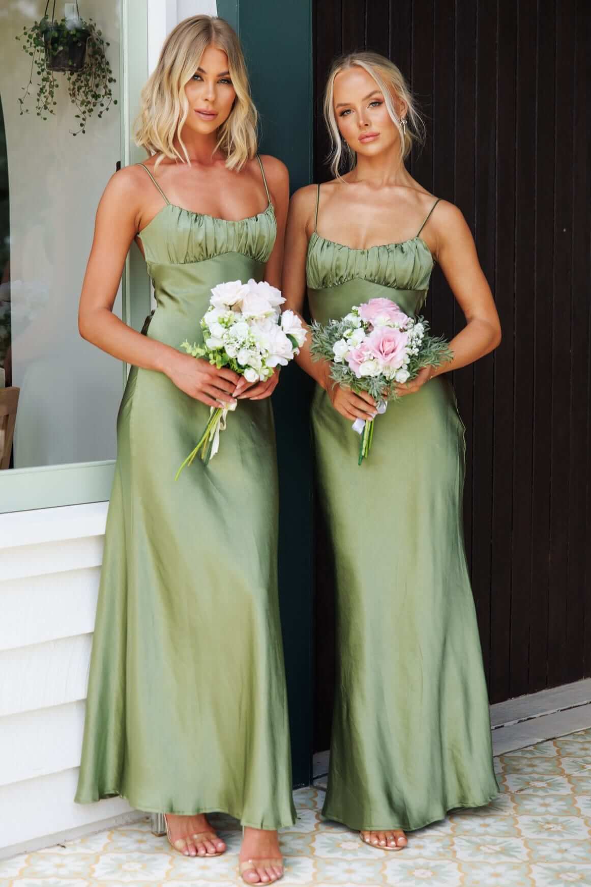 Two women in green Celine Maxi Dresses holding bouquets, showcasing adjustable straps and gathered bust design.