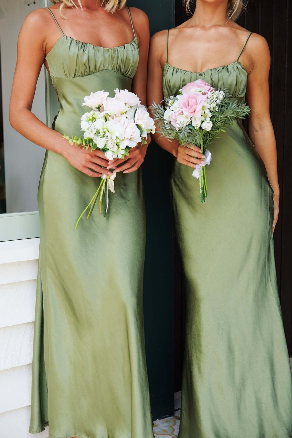 Two women in olive green satin Celine maxi dresses holding flower bouquets, showcasing adjustable straps and elegant fit.