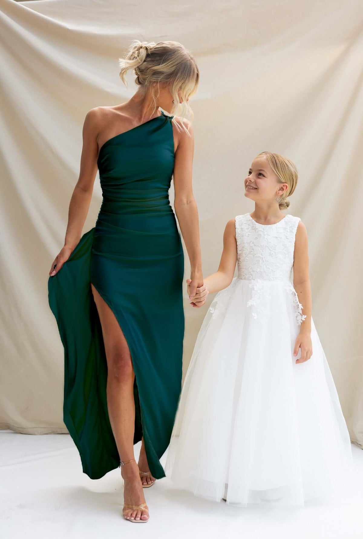 Woman in green satin Dimmi Maxi Dress with side slit, holding hands with girl in white dress, set against a neutral backdrop.