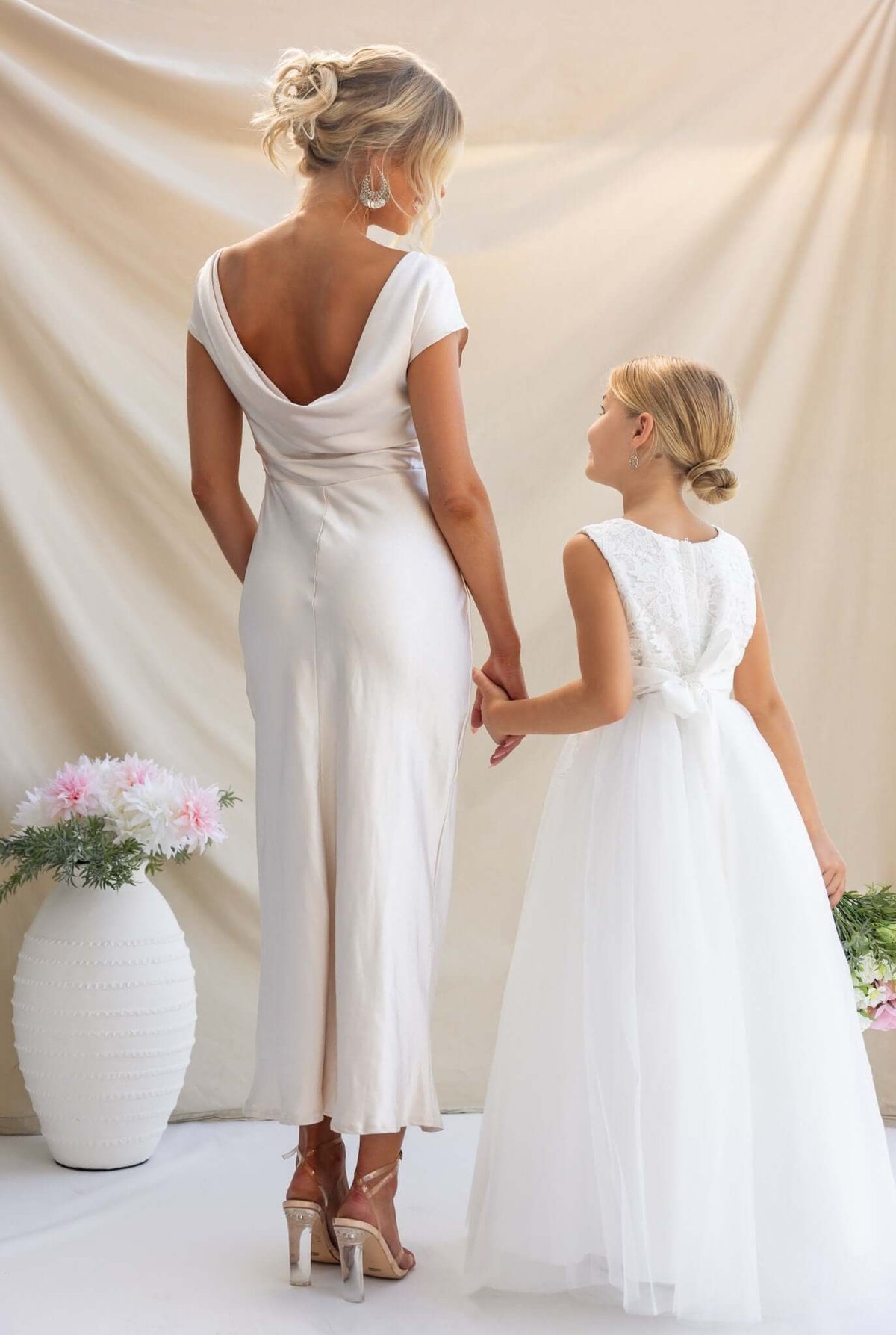 Woman in an Esmeralda Maxi Dress with off-shoulder design, holding hands with a girl in a white dress, against a soft backdrop.