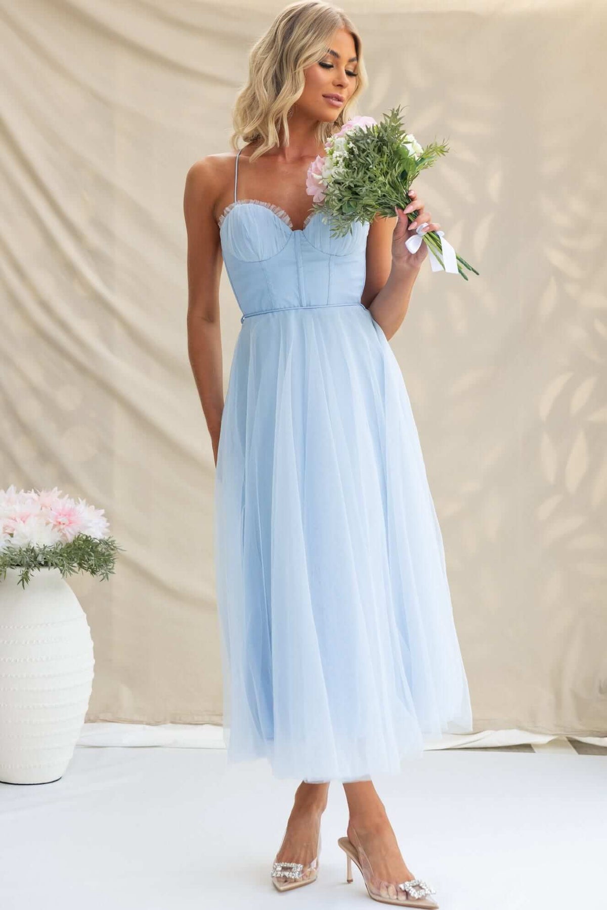 Light blue Florence Midi Dress with adjustable straps, tulle fabric, and floral bouquet in hand.