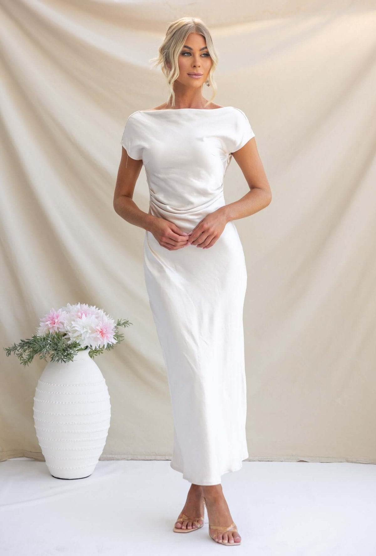 Model wearing Esmeralda Maxi Dress with boat neckline and draped back in satin fabric, styled with minimal accessories.