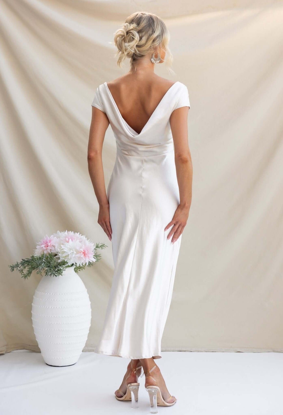 Elegant Esmeralda Maxi Dress with boat neckline, draped back, showcasing satin material in a charming setting.