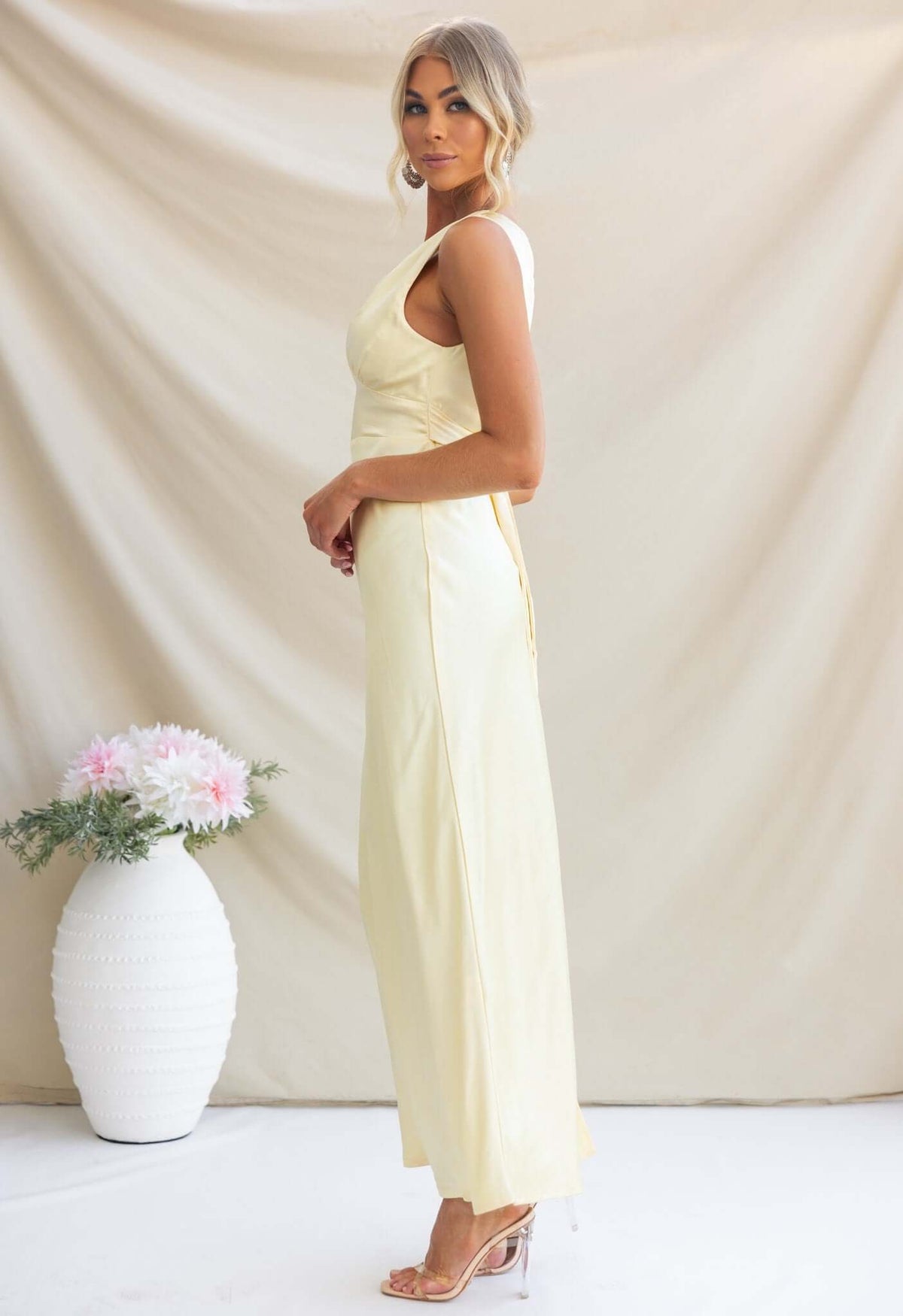 Elegant Alika Maxi Dress in soft yellow, featuring a V-neckline and split at the back, styled with a chic hairdo.