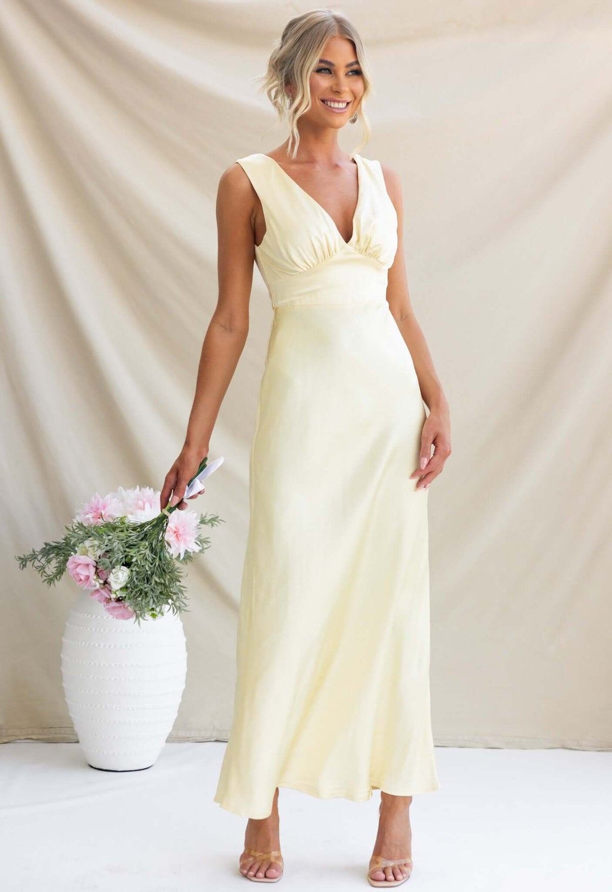 Alika Maxi Dress in soft yellow with V-neckline and split at back, styled with fresh flowers.