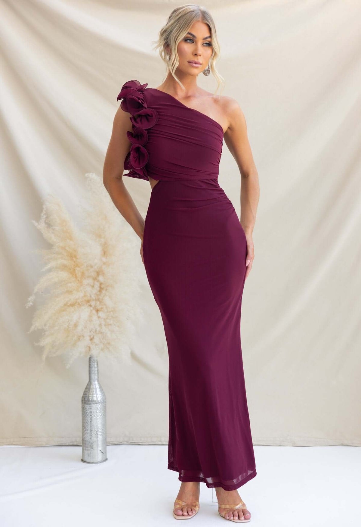 Model wearing burgundy Meriden Maxi Dress with one-shoulder neckline and floral detail, showcasing elegant evening wear.