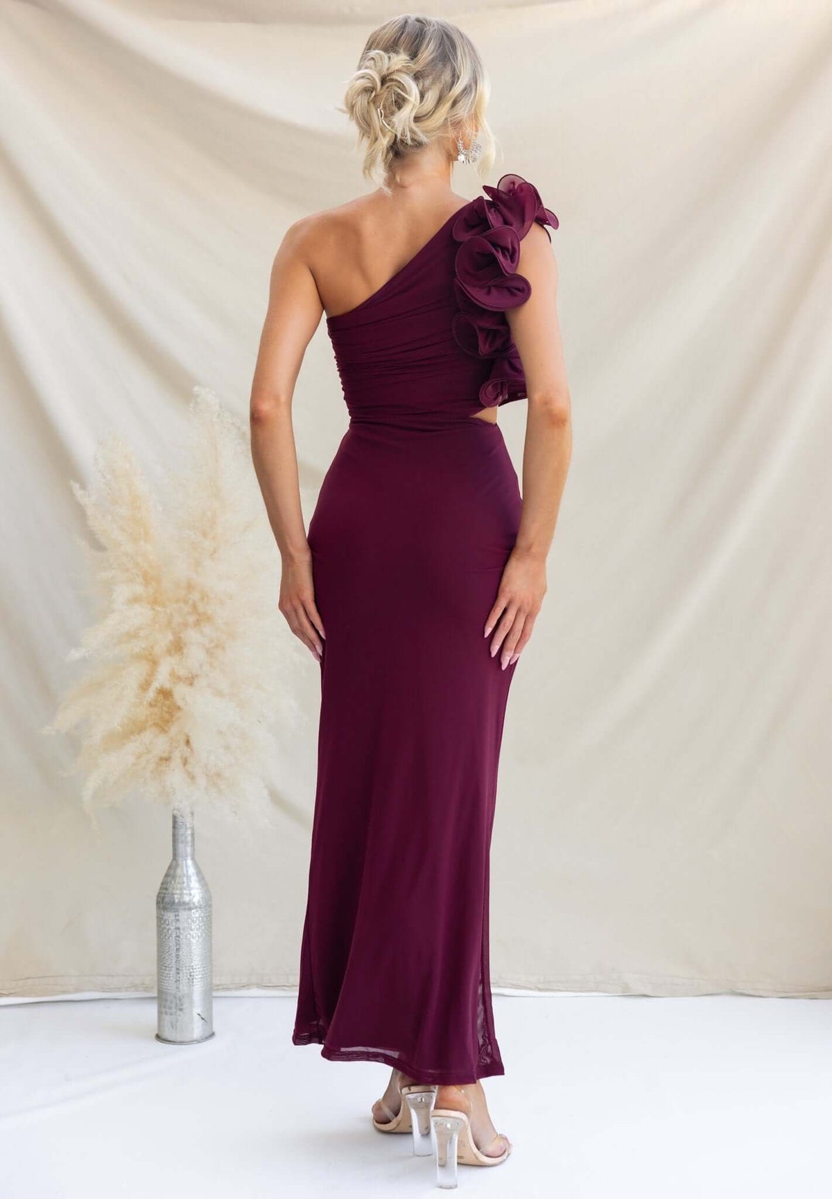Back view of a burgundy Meriden Maxi Dress with one-shoulder design and ruffled detail, styled elegantly.